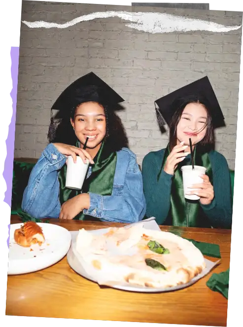 Two smiling graduates in caps and gowns celebrating with drinks