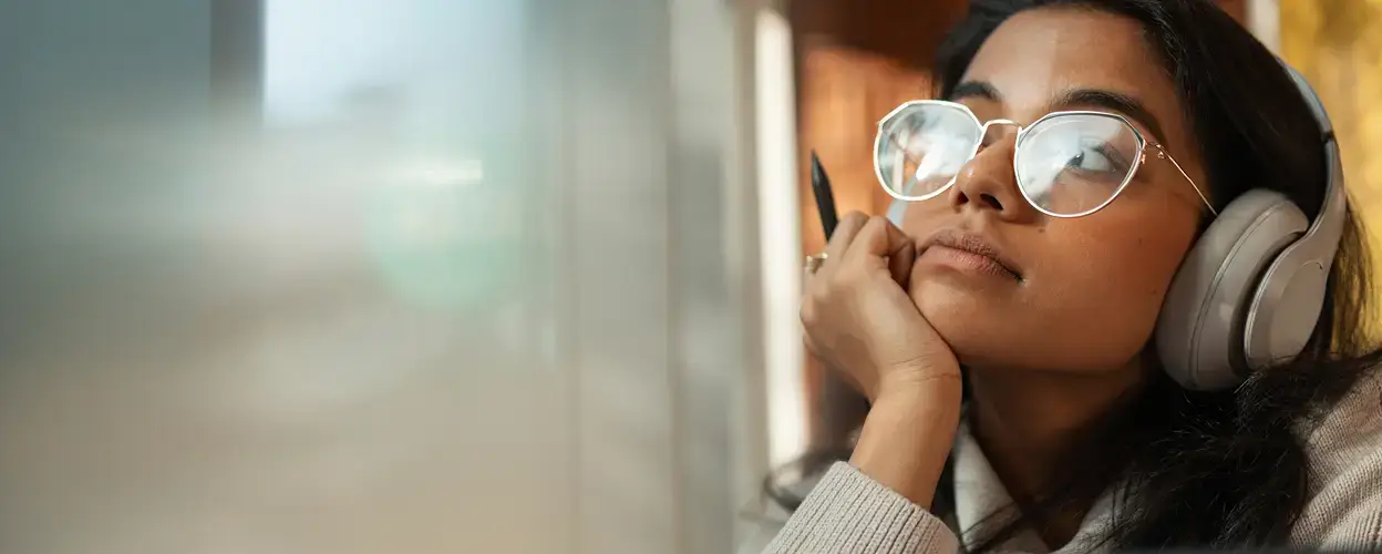 A girl wearing wire-rimmed glasses and over-ear headphones while thinking