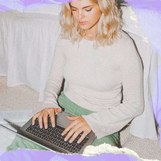 A girl wearing a cream-colored top working on a laptop